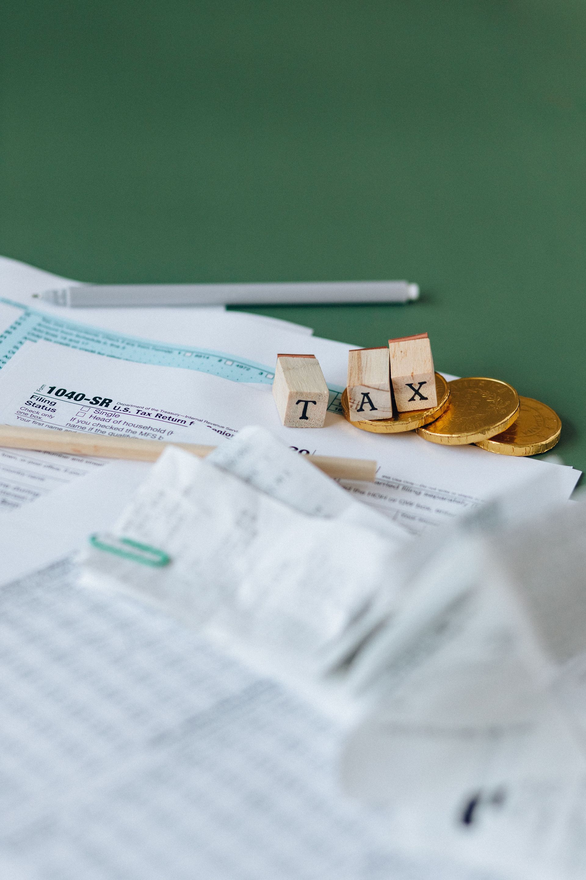 Tax forms, coins, and block letters spelling 'TAX' on a green background, symbolizing finance.